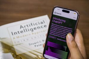 close up of a smartphone displaying chatgpt app held over ai textbook